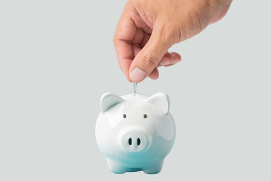 A hand placing coins into a piggy bank.